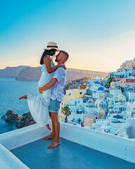 Fototapeta na wymiar Santorini Greece, a young couple on luxury vacation at the Island of Santorini watching the sunrise by the blue dome church and whitewashed village of Oia Santorini, Asian women and caucasian men