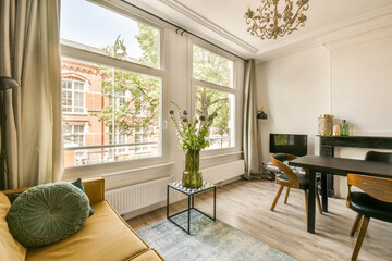 a living room with a table, chairs and a tv in the corner of the room looking out onto the street