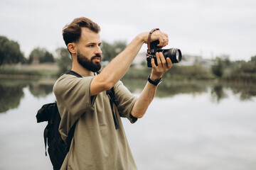 a young man with a modern SLR camera in his hands on a natural background - obrazy, fototapety, plakaty