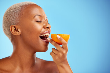 Orange, skincare and nutrition with a model black woman in studio on a blue background biting...
