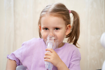 Cute little girl inhaling mist form nebulizer at home. Holding mask over her nose and mouth 