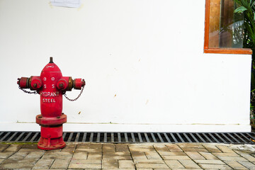 Red steel hydrant pump placed outdoors with a white wall as the setting