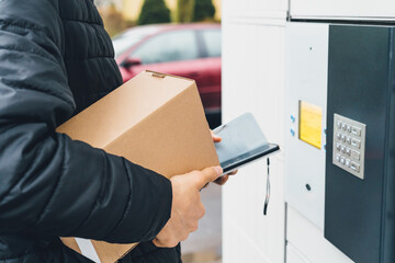 A man with smartphone, box in hands near the self-service mail terminal. Parcel delivery machine....