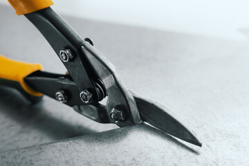 closeup of metal scissors cutting a tin sheet - obrazy, fototapety, plakaty