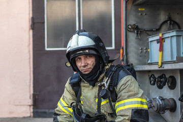 Portrait of a tired firefighter in a protective suit and a protective helmet sitting by a fire...