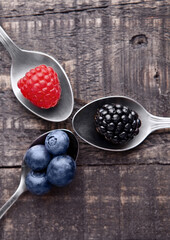 Raspberry blueberry and blackberry on spoon and wooden table. Still life photography
