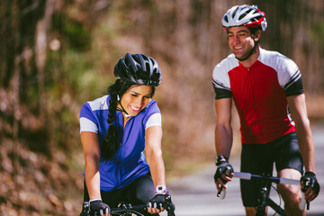 A laughing young couple wearing blue and red jerseys bike together on a trail in the woods