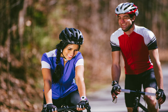 A laughing young couple wearing blue and red jerseys bike together on a trail in the woods