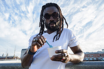 young man of African ethnicity outdoors enjoying a small cup of ice cream at sunset