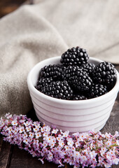 Blackberry in white bowl and flowers on wooden background. Natural healthy food.Still life photography