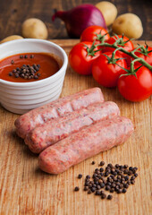 Raw beef sausages with tomatoes and sause on kitchen wooden board. Potatoes and pepper