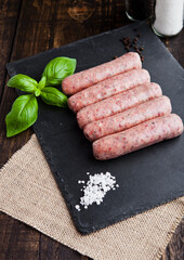Raw beef sausages with salt and basil on stone board.Dark brown board. Salt and pepper on background