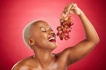Happy, eating and black woman with grapes on a red background for nutrition, diet or health. Smile, beauty and an African model or girl with fruit, hungry and food for a detox isolated on a backdrop