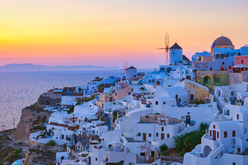 sunset with white churches an blue domes by the ocean of Oia Santorini Greece, a traditional Greek...