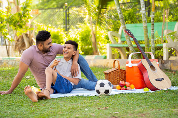 Happy indian father with son spending time together at picnic park during weekend holidays -...