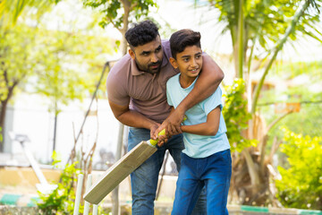 indian father teaching his son to playing cricket game at park - concept of Shared passion, family bonding and fatherhood