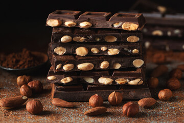 Dark and milk chocolate with nuts on a dark background sprinkled with cocoa powder.