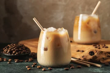 Ice coffee in a tall glass with cream poured over, ice cubes and beans on a dark concrete table. © Vasiliy