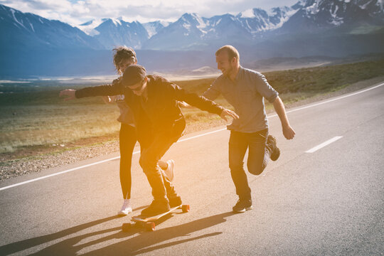 Group of friends run, laugh and having fun. The guy on longboard. Asphalt road.