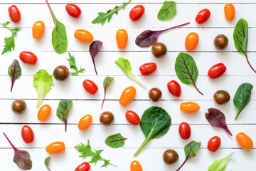 Various fresh green salad leaves and colorful cherry tomatoes on white wooden background. Flat lay. Top view