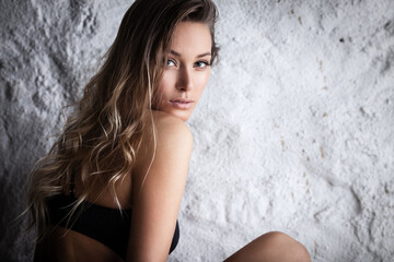 Naklejka premium Fashion portrait of beautiful female model posing in black lingerie near white wall