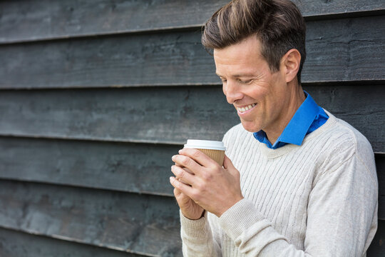 Portrait shot of an attractive, successful and happy middle aged man male outside drinking coffee in a disposable takeaway cup.