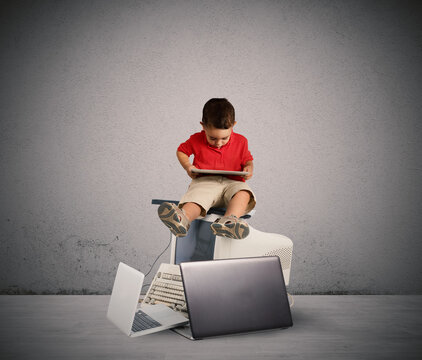 Child sitting on a pile of computers. Harmful technology for the growth of the child concept
