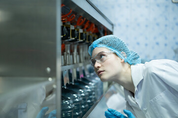 Female scientist in white coat and blue hat working in the control  machine of production line.