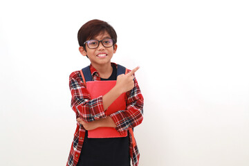 Happy asian student holding a book while pointing sideways. Isolated on white