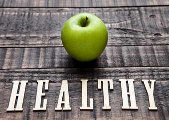 Green organic healthy apple on wooden board. With letters below