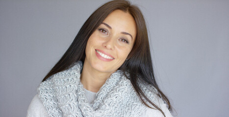 Obraz premium Gorgeous brunette woman posing isolated on gray background. She wearing sweatshir and woolen warm scarf. She is full of happiness. With a big smile on her face.