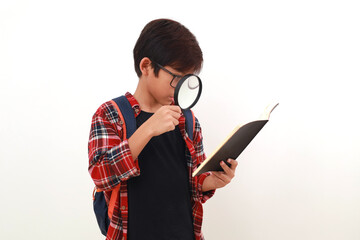 Happy smart asian student holding a book while looking through a magnifying glass. Isolated on white