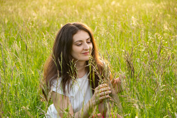 Young woman admiring the nature of field grass in summer. The unity of people and nature