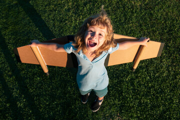 Amazed child playing with toy plane wings in summer park. Kid dreams of future. Kid pilot dreaming....