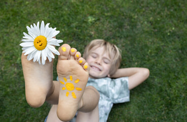 Chamomile flower between toes of bare foot of happy child lying on grass. cheerful positive atmosphere, childhood. Hello summer. rest, pampering, the energy of nature. Earth Day. selective focus