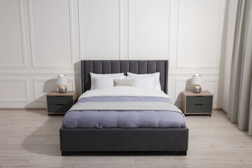 Comfortable bed between bedside tables with lamps at home. Interior design