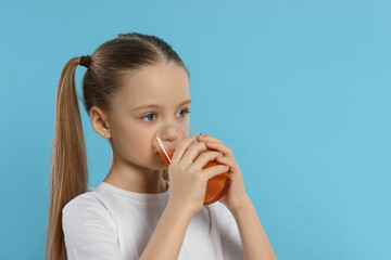 Little girl drinking fresh juice on light blue background, space for text