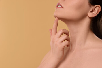Fototapeta na wymiar Young woman massaging her face on beige background, closeup. Space for text