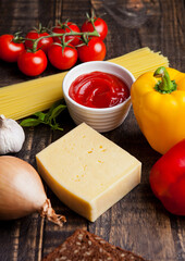 Raw food mix spaghetti tomatoes cheese and bread on wooden table