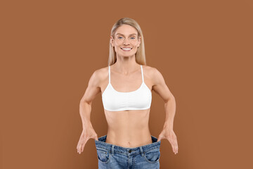 Slim woman wearing big jeans on brown background. Weight loss