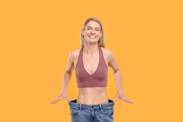 Slim woman wearing big jeans on yellow background. Weight loss