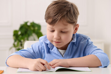 Little boy erasing mistake in his notebook at white desk indoors