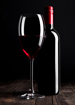 Red wine bottle and glass on wooden table black background