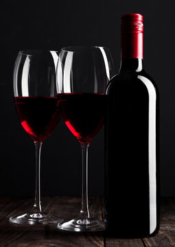 Red wine bottle and glasses on wooden table black background