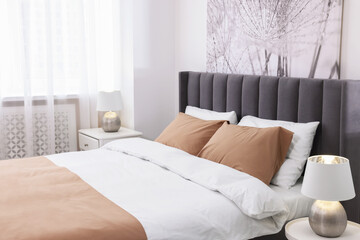 Comfortable bed and lamps on bedside tables in light room. Stylish interior