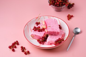 Summer refreshing dessert, sliced Italian semifreddo ice cream with red currants in a red and white plate on a pink plain background. Ice cream recipes.