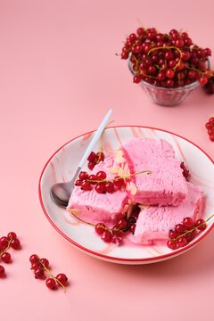 Summer refreshing dessert, sliced Italian semifreddo ice cream with red currants in a red and white plate on a pink plain background. Ice cream recipes.