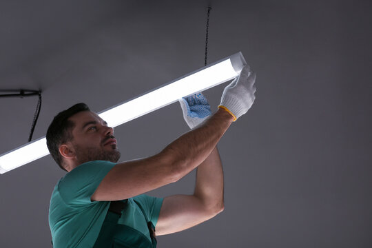 Ceiling light. Electrician installing led linear lamp indoors, low angle view. Space for text