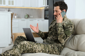 Soldier with laptop talking on phone at home. Military service