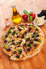 Delicious pizza background. Fresh pizza, garlic, olive oil, fresh herbs, tomatoes, artichokes and black olives on wooden background.